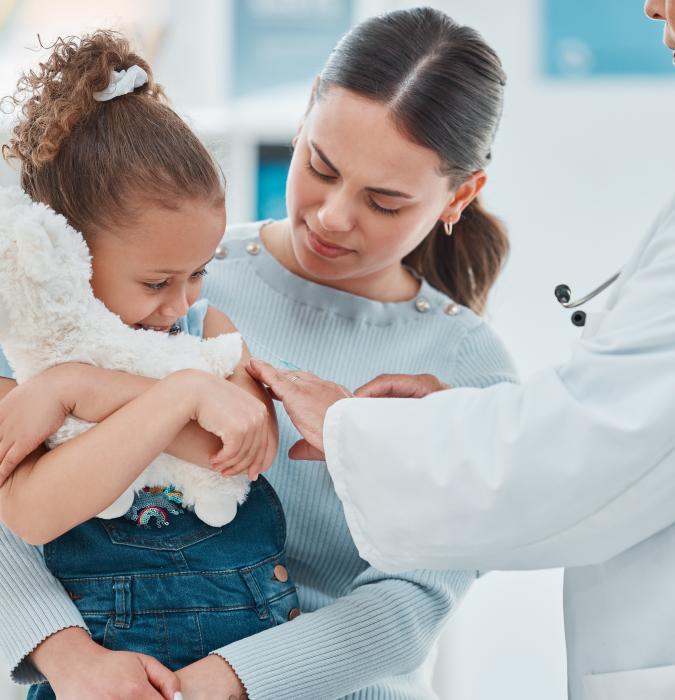 A little girl hugs her stuffy while visiting with her doctor and mother.