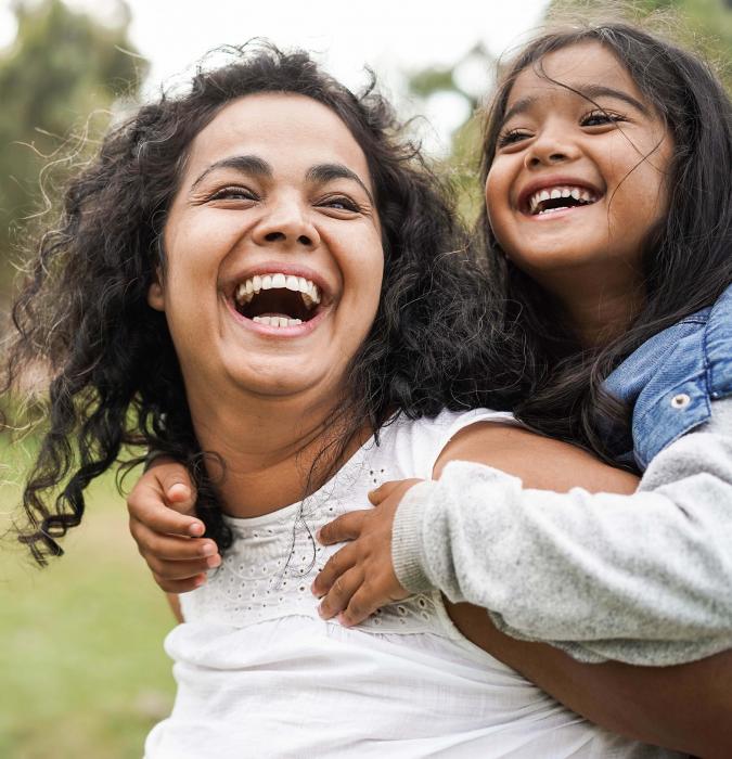 Mother and daughter laughing together while playing outside. 